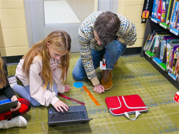 student and teacher working on robot in library